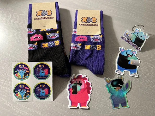 Socken, Sticker und Monster-Schlüsselanhänger mit Studio4Kids-Branding liegen auf einem Tisch