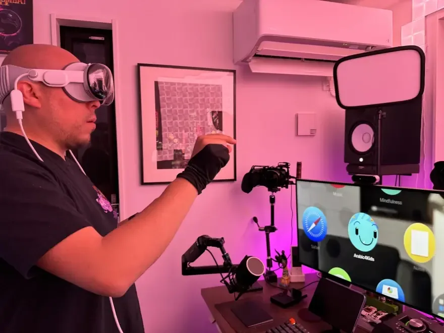 رجل يرتدي سماعة Apple Vision Pro يمد يده نحو شاشة تعرض تطبيق Arabic4Kids