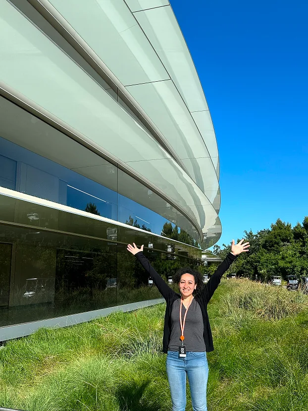 Sylvia Said reckt freudig die Arme vor dem geschwungenen Glasgebäude des Apple Park